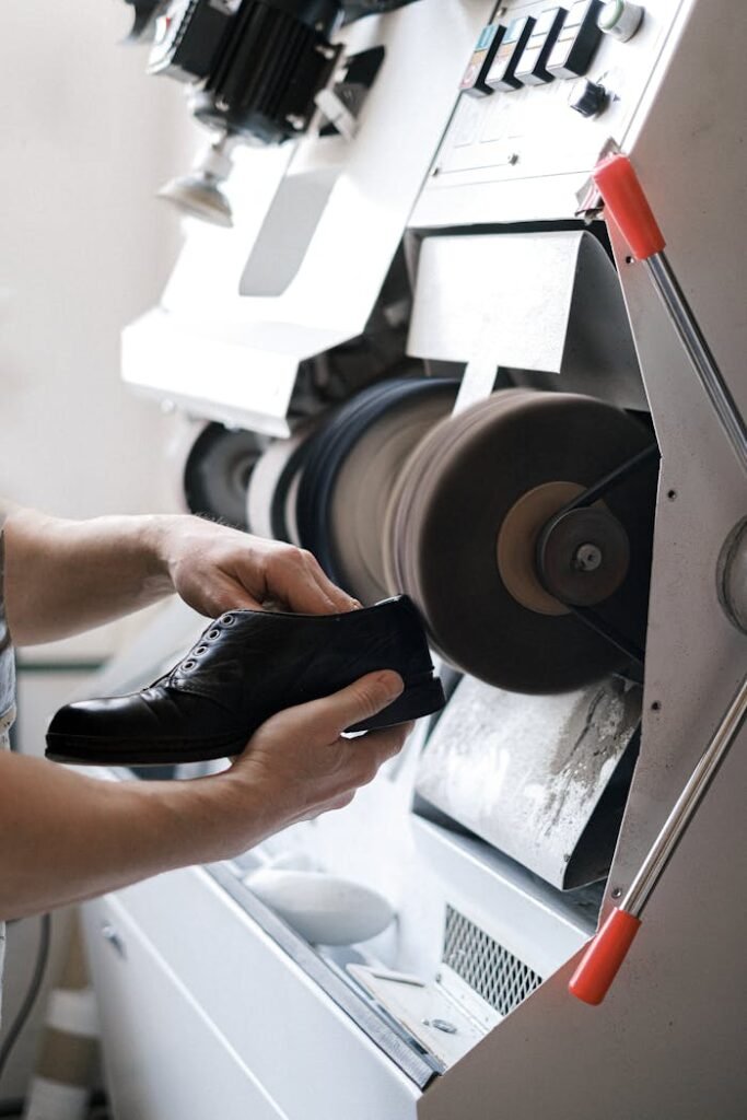 zipwp-image-5894227 Close-up of craftsman polishing a leather shoe using industrial machinery indoors.