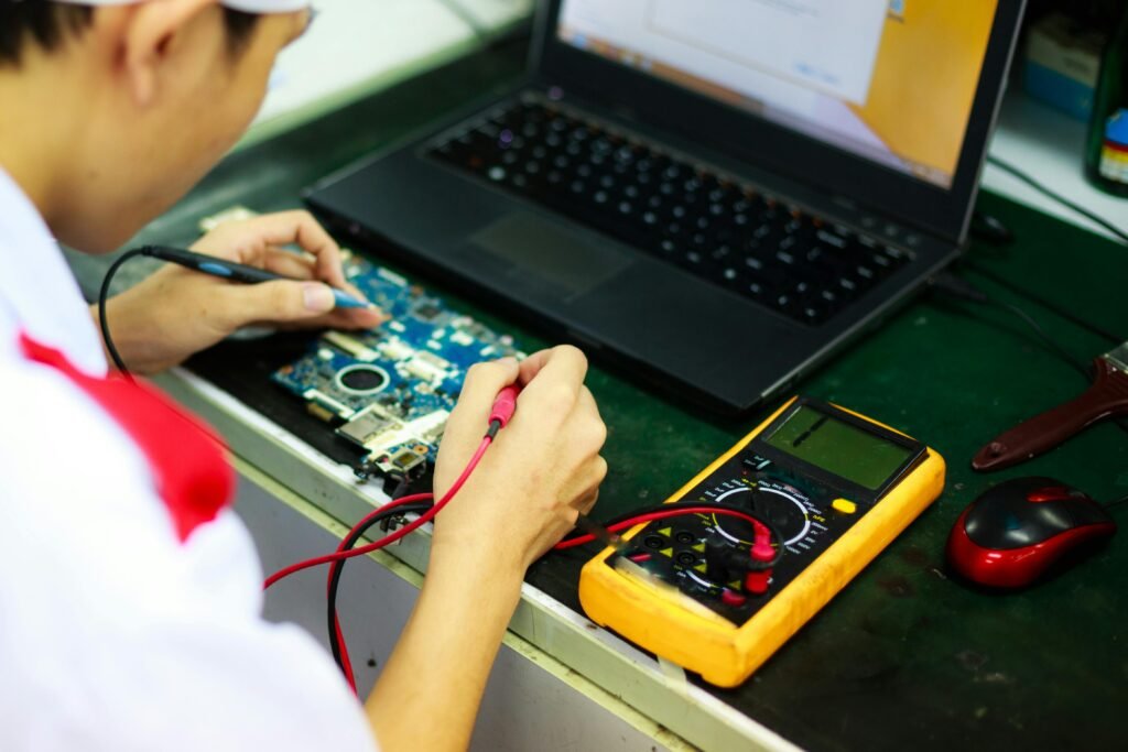 pexels-photo-2136243-2136243 Technician working on a laptop with multimeter in a professional workspace.